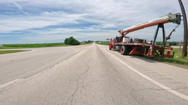 POV while driving on flat country road through rural Illinois; driving past homes, farms and truck with a crane; concepts of open road, rural life and transportation