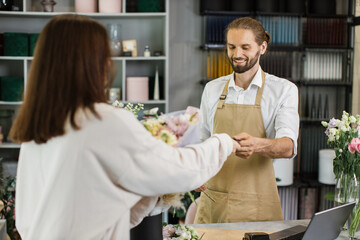 Hadsome bearded male florist receiving discount card from regular female customer and making payment at terminal in flower shop.