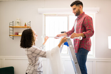 Happy man helping his partner to put the curtains on the new house