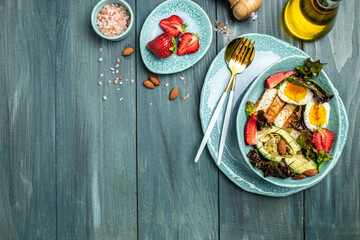 Ketogenic low carbs diet, Plate with keto foods: two eggs, avocado, grilled chicken fillet, nuts, strawberries and fresh salad. Healthy fats, clean eating for weight loss. top view