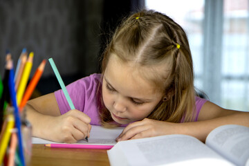 Back to school. A cute little blonde girl is doing her homework in a working school notebook with...