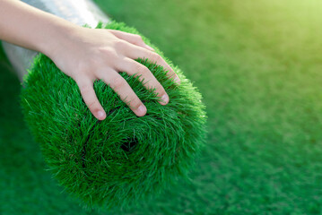 Selective focus of a hand stroking a roll of soft, squishy artificial turf. Economical green lawn...