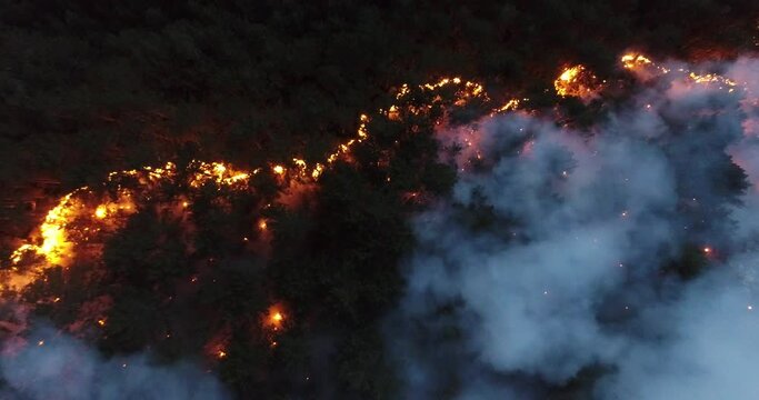 Aerial panoramic view of a forest fire at night, heavy smoke causes air pollution, and fire in full blaze. Natural disaster epic drone cinematic shot.