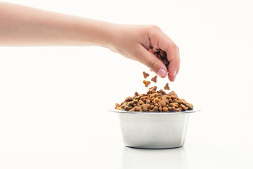 A woman's hand pours dry food for cats and dogs into a bowl for pets