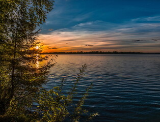 Fototapeta na wymiar Sunset over a blue lake with green trees on the shore