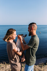 Happy couple with favourite pet. Young man and woman have walk near sea.