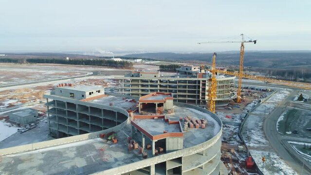Building materials on roof of future office center and cranes at construction site against field on winter day aerial view