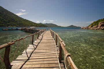 The scenery of wooden bridge to the port from south of Thailand.  The wooden bridge in the sea with blue sky and mountains.