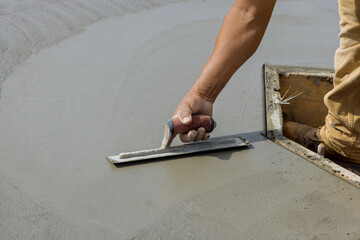 Masonry worker holds a trowel as he smooths out plastering concrete on top cement floor with the help of steel trowel