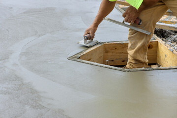 On the new cement floor, construction worker is using a stainless steel edger to form corner with the wet cement
