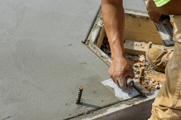 A masonry worker holds a steel trowel and is smoothing a cement floor with plastering concrete that...