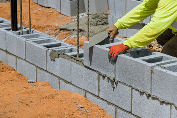 A mason is placing the aerated concrete blocks on the wall as he lays the mounting parts on...