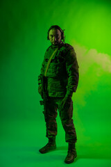 soldier in the studio on a green background with colored light. a man in military uniform with a gun, rifle or machine gun. military. airball player