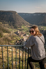 Fototapeta na wymiar Junge Frau besucht Baume-les-Messieurs, Bourgogne-Franche-Comté und schaut auf ein alte schönes Dorf in Frankreich zwischen beeindruckenden Felswänden
