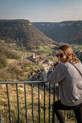 Junge Frau besucht Baume-les-Messieurs, Bourgogne-Franche-Comté und schaut auf ein alte schönes Dorf in Frankreich zwischen beeindruckenden Felswänden