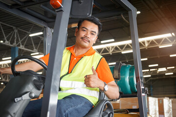 Happy and satisfied Asian worker in warehouse sitting a forklift and showing a thumb up to camera.