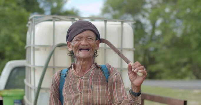 Happy smiling Asian male farmer more than sixty years old with a syringe tank on his back and works as a wage earner in a farm,smiling and laughing happily.