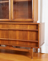 Warm wooden mid-century modern credenza hutch. Detail view of vintage sideboard before a long white curtain. 