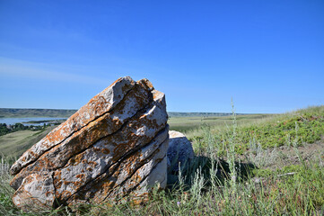 blue skies and a large splitting lichen covered sandstone rock on a  green hillside of a valley