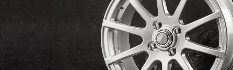 a fragment of a sports alloy wheel in silver color on a gray background. copy space empty space for text panoramic photo