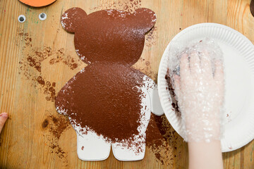 DIY home made paper Teddy bear with bubble wrap film painting technique and pom pom balls glued on the tummy. in picture visible kid parts of body.