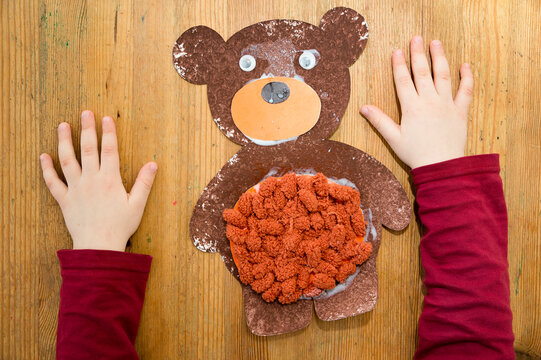 DIY home made paper Teddy bear with bubble wrap film painting technique and pom pom balls glued on the tummy. in picture visible kid parts of body.