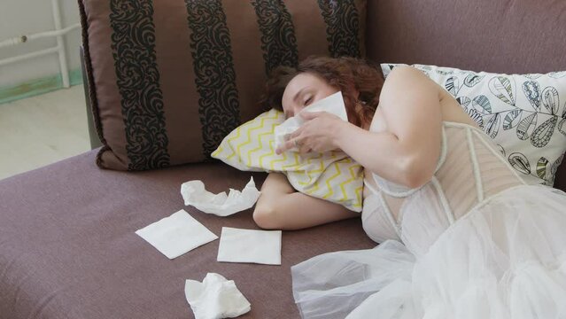 4K. Sad bride in a white wedding dress crying on the couch