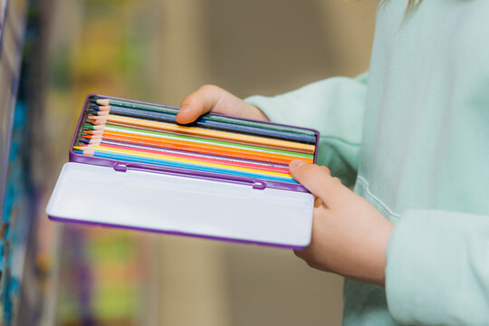 partial view of child holding set of new color pencils.