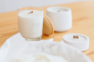 Obraz na płótnie Canvas Trendy White Soy Candle with Empty Label Holder. Handmade Candle Stands on Wooden Table.