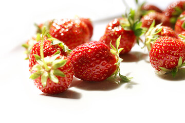 Fresh strawberries with leaves are scattered on the plate  at the top right corner of the white background. Side View. Close-up. Copy Space