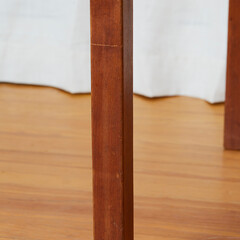 Rich brown teak mid-century modern dining room table. Leg close-up view with white drapes in the background. 