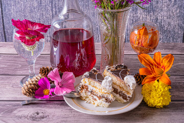Summer still life with bottle of wine,  vase, slices of cake in plate and wine glasses with water and flowers on dark wooden background.