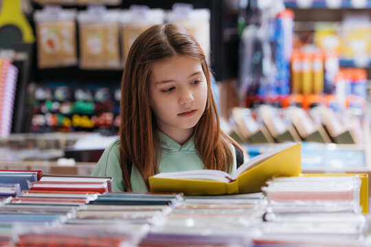 girl looking at new copybook in stationery store on blurred foreground.