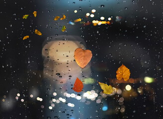 Rainy  weather Autumn leaves on window rain drops and Autumn leaves fall night city traffic blurred light colorful reflection cold season background 