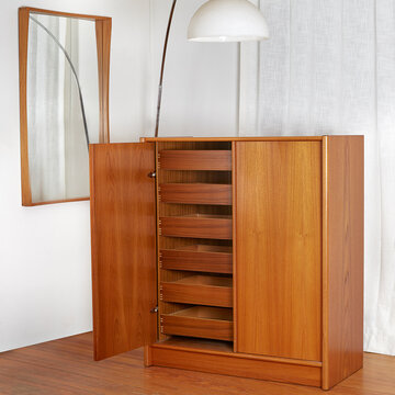 Interior of a luxury home with white walls, mid-century furnishings, lamp, Danish Teak Gentleman's Chest, and teak frame mirror. 