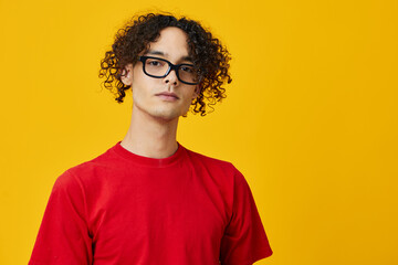 Fototapeta na wymiar Lovely myopic young student man in red t-shirt funny eyewear looks at camera posing isolated on over yellow studio background. The best offer with free place for advertising. Education College concept