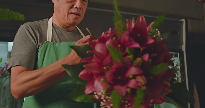 A small business employee of flower shop creating a bouquet of flowers arraignment. An Asian American entrepreneur creating artisan bouquet for client