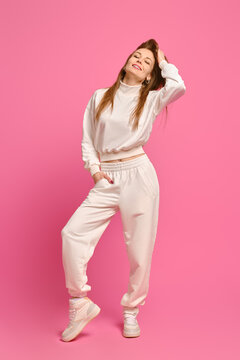 Active woman in white fleece sweatshirt and sweatpants posing over bright pink background