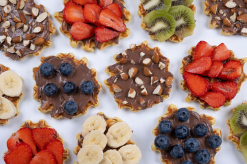 background of appetizing sweet wafers with chocolate spread, nuts and fruits on a white background. Summer, bright, trendy background, food design