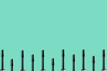 Set of many black mascara brushes with sharp shadows isolated on green mint background with copy space. Beauty product smear pattern. .