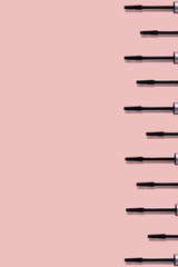 Set of many black mascara brushes with sharp shadows isolated on pink background with copy space. Beauty product smear pattern. .