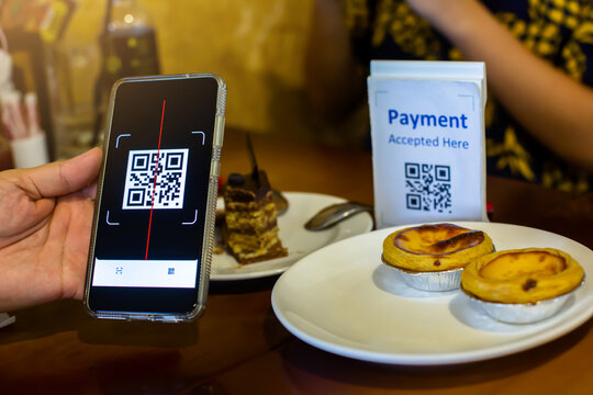 Customer hand using smart phone to scan QR code Tag with blur egg tart or desseart in coffee shop or restaurant to accepted generate digital pay without money.