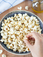 Human hand picking popcorn from a bowl on a wooden table. Top view, a closeup. Healthy homemade vegan snack. 