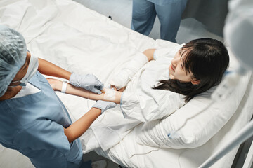 Horizontal high angle view shot of young Asian woman getting intravenous therapy in emergency room