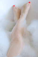 female legs in soapy foam in a white bath