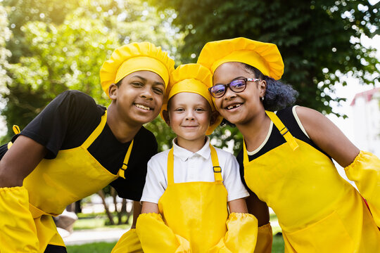 Multiracial company of children cooks in yellow uniforms smile outdoor. African teenager and black girl have fun with caucasian child boy and cook food. Kids portrait.