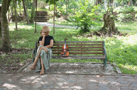 Woman wearing woven hat sitting on old and rust bench,at the left side,beside violin