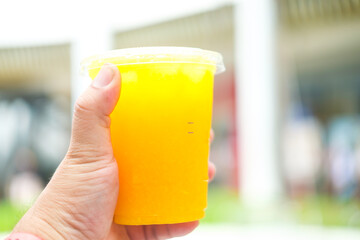Hand is holding plastic glass on orange juice