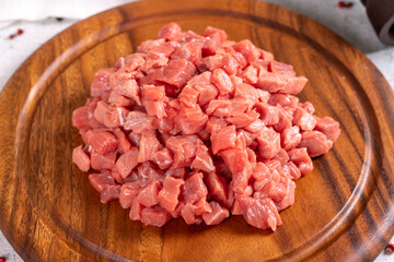Cubed meat. Chopped red meat in a wooden serving dish on a stone background. Butcher products. close up