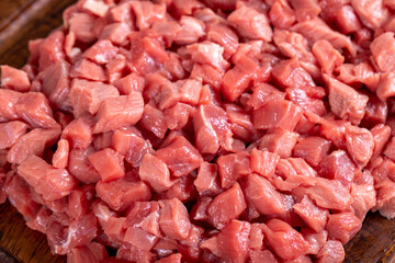 Cubed meat. Chopped red meat in a wooden serving dish on a stone background. Butcher products. close up